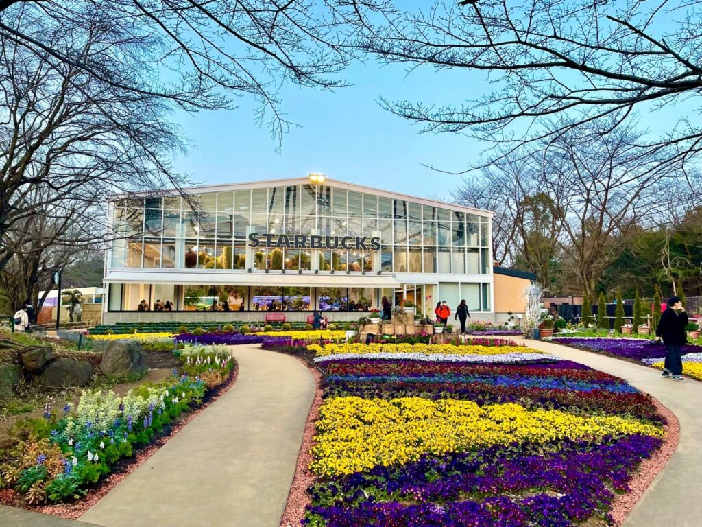 A garden with many colorful flowers in front of a glass building at Hanabiyori Flower Park.