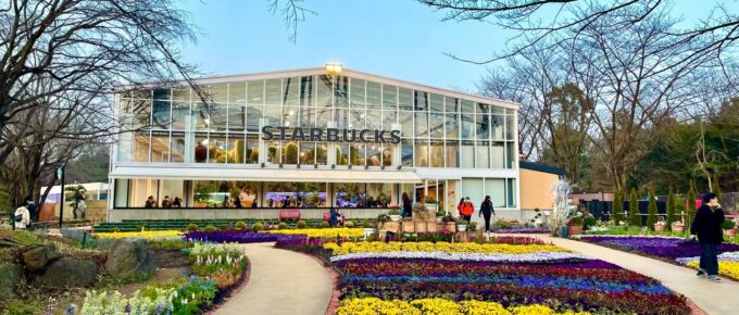 A garden with many colorful flowers in front of a glass building at Hanabiyori Flower Park.