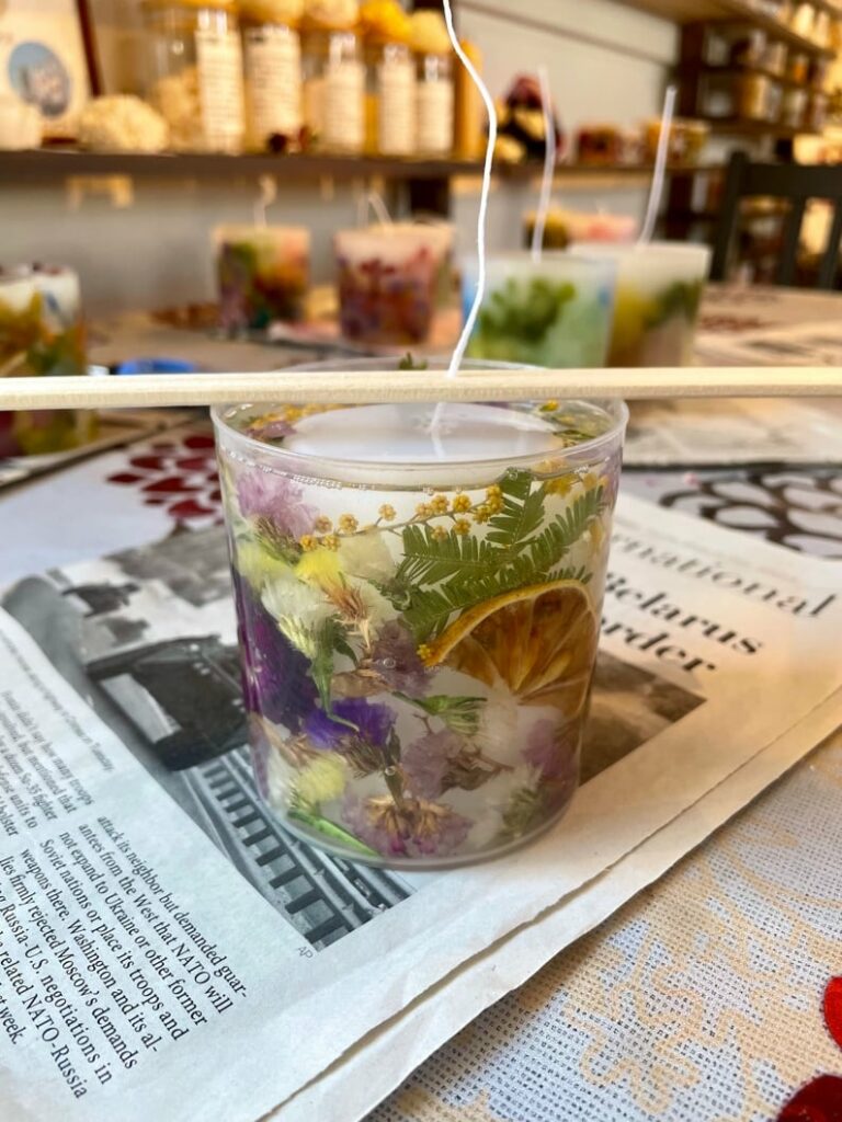 A candle with flowers and leaves on top of a table.