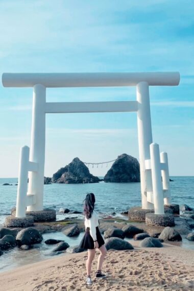 A woman standing on the beach next to a tori tori gate.