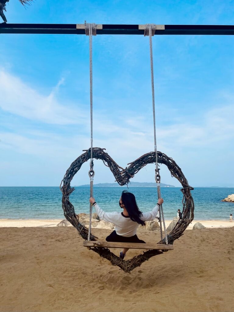 A woman on a swing in the shape of a heart on a beach.