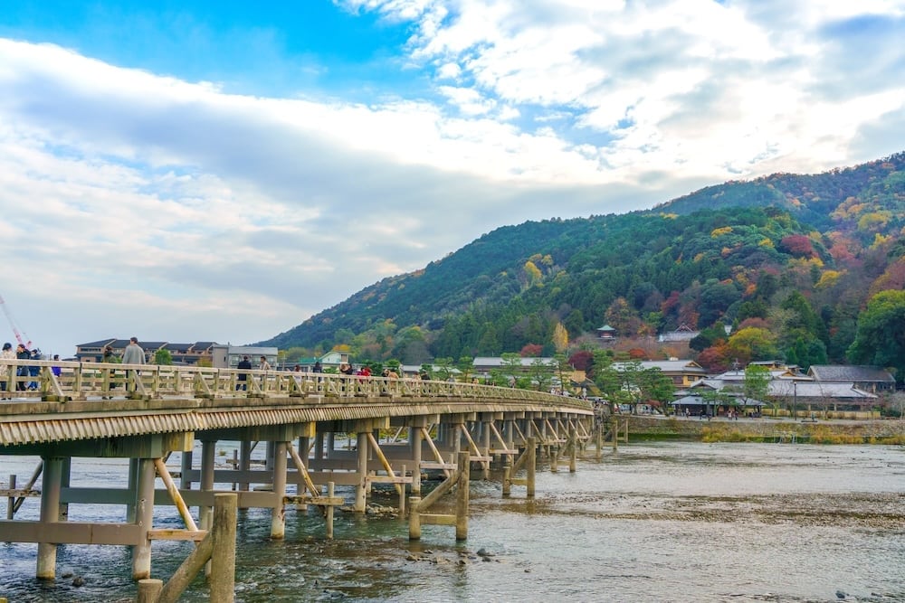 A wooden bridge over a river with mountains in the background.