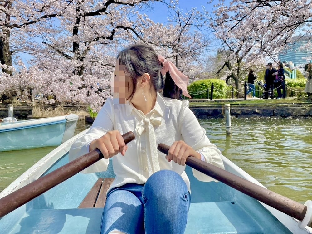 A woman is rowing a boat in a pond surrounded by cherry blossoms.