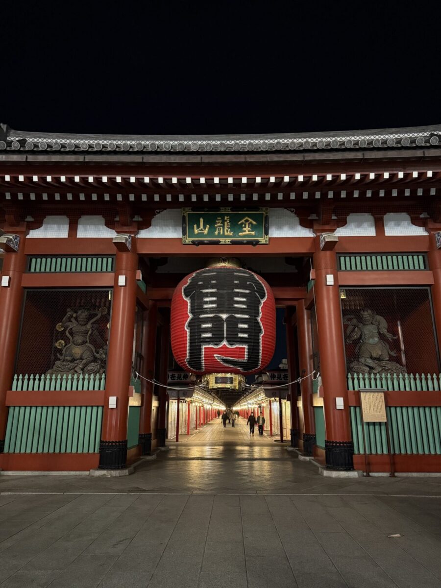 Night view of the Kaminarimon Gate at Senso-ji Temple in Tokyo, featuring a large red lantern and two statues on either side.